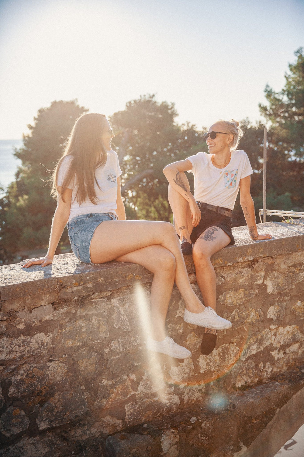 Zwei Freundinnen mit Pocket Shirts auf einer Mauer im Abendlicht