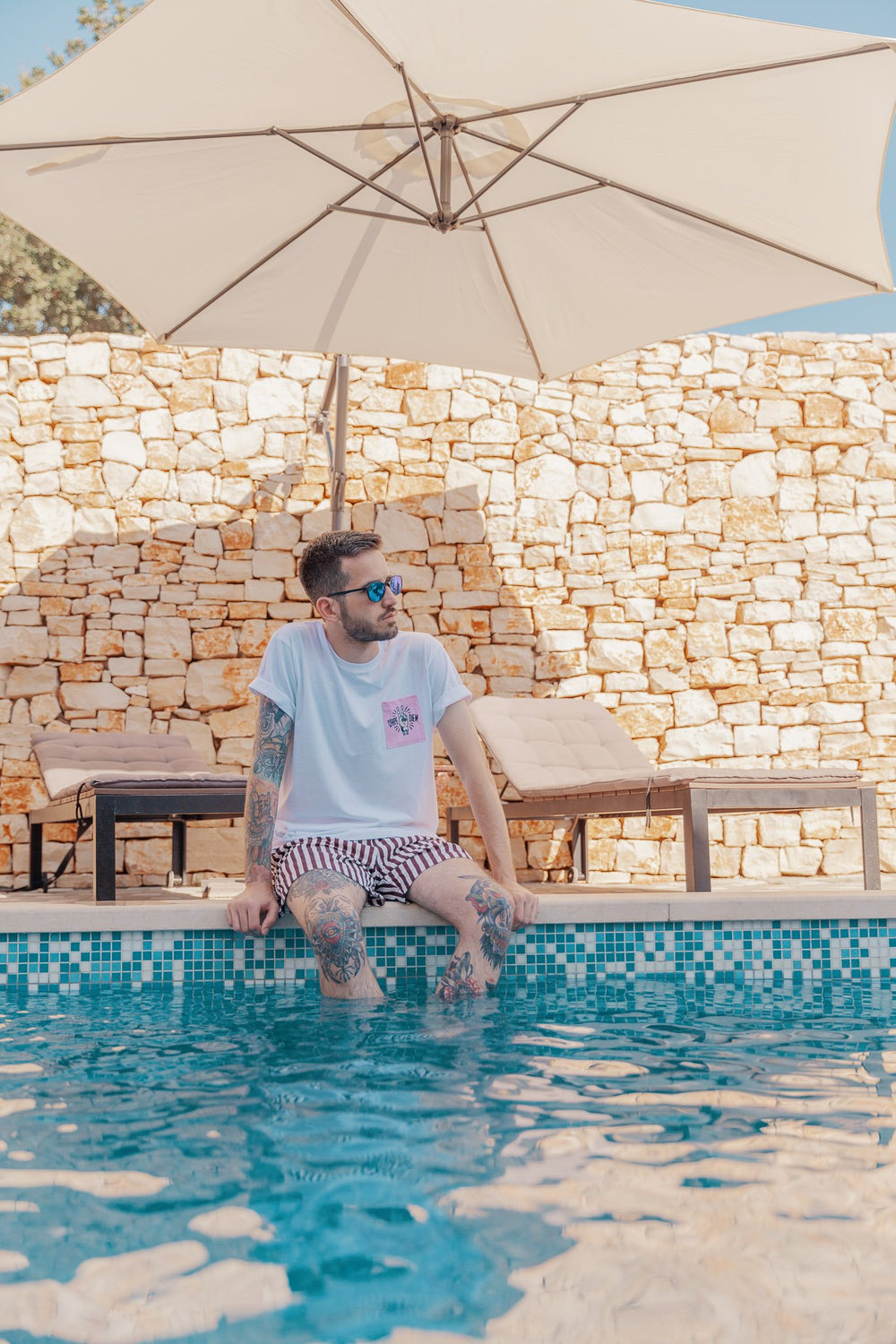 Mann im Pocket Shirt am Pool unter einem Sonnenschirm
